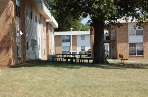 a picnic table sits under a tree in front of a brick building