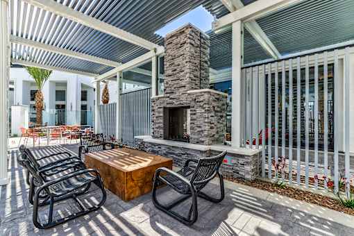 A patio with a stone fireplace and black metal chairs.