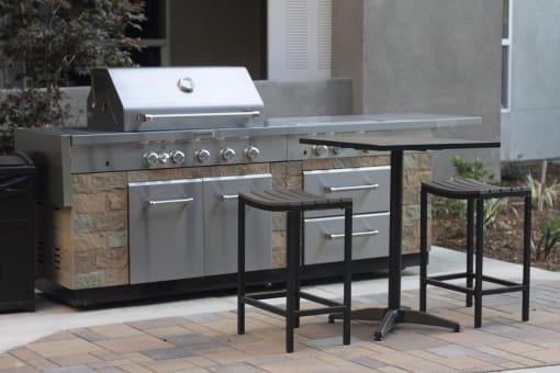 an outdoor kitchen with a grill and bar stools at The Crossings at Redlands, Redlands, CA