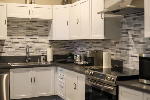 a kitchen with white cabinets and black countertops at The Crossings at Redlands, Redlands, CA