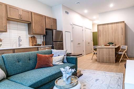A blue couch with a red pillow is in the middle of a kitchen and living room.