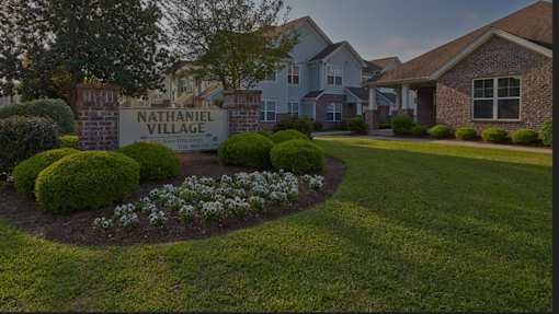 A sign that says Nathaniel Village Rittenhouse is in front of some houses.