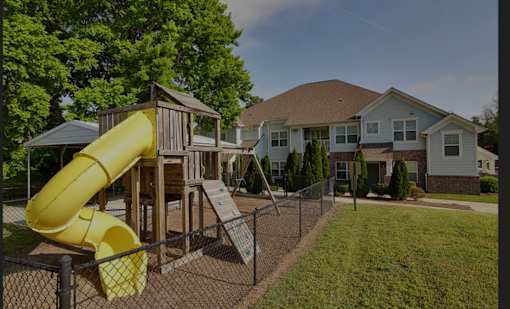 A playground with a yellow slide in front of a house.