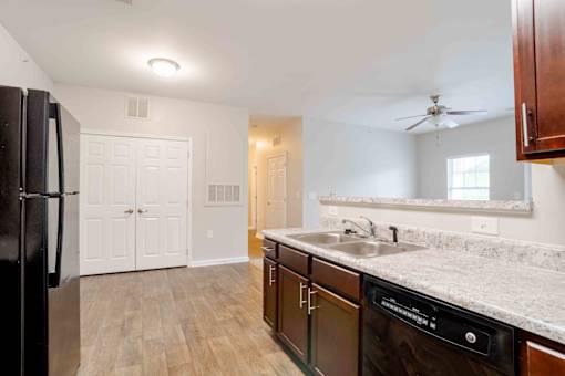A kitchen with a black fridge, white cabinets, and a marble countertop.