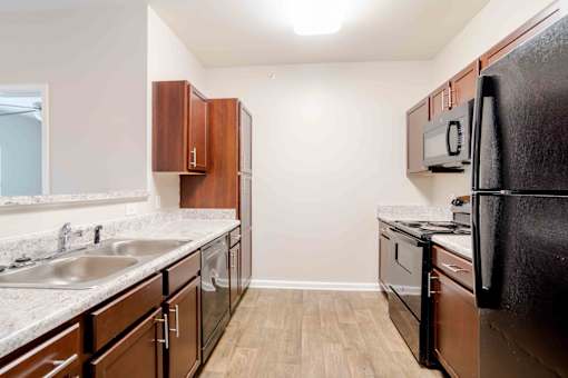 A kitchen with a black refrigerator, brown cabinets, and a white countertop.