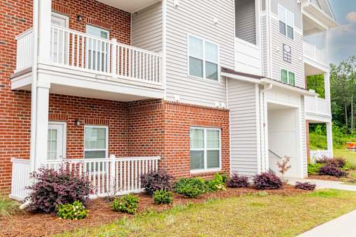 A two-story apartment building with a balcony and a small garden in front.