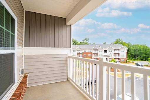A balcony with a white railing and a view of a parking lot and buildings.