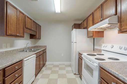 A kitchen with white appliances and brown cabinets at Carriage Hills, NC 28358