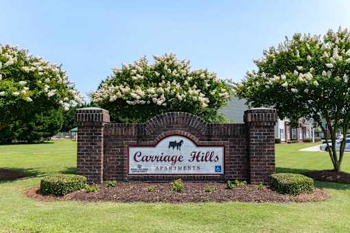 A sign for Carriage Hills Apartments is surrounded by bushes and trees at Carriage Hills, 28358