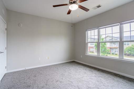 Large bedroom with neutral tones, carpet flooring, ceiling fan, and oversized windows offering abundant natural light at Cedar Terrace Apartments in Hendersonville, NC 28792