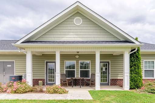 Inviting clubhouse exterior with covered front porch, patio seating, and manicured landscaping at Cedar Terrace Apartments in Hendersonville