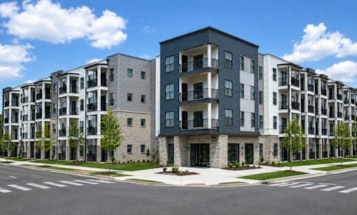 A row of modern apartment buildings with balconies and trees in front.