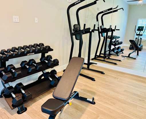 A gym with a variety of equipment including dumbbells, weight plates, and a bench.