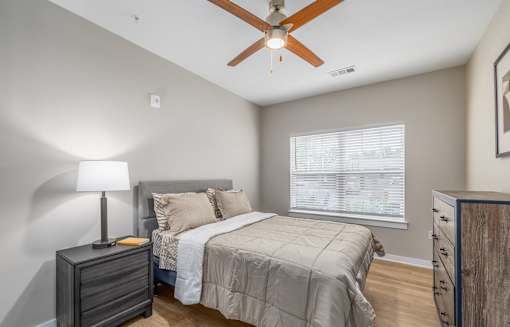 A bedroom with a bed, dresser, and ceiling fan.