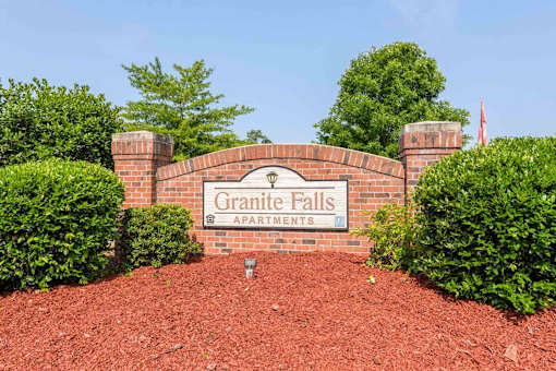A sign that says Granite Falls Apartments stands in front of a hedge.