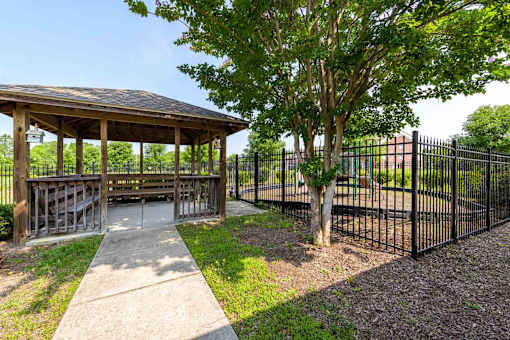 A gazebo is surrounded by a black fence and a tree.