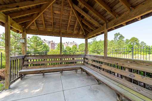 A wooden pavilion with a bench and a fence in the background.