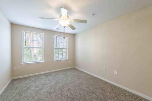 A room with a ceiling fan and two windows.