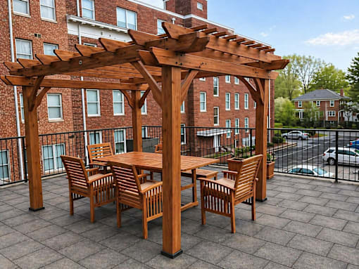 A wooden pergola with a table and chairs is set up on a patio.