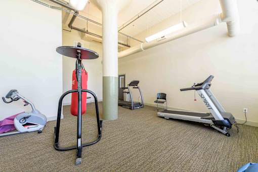 A gym with a treadmill, a stationary bike, and a weight machine.at Mebane Mill Lofts, Mebane, NC 27032
