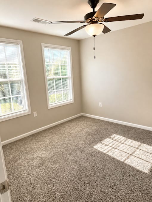 A room with a ceiling fan and two windows.