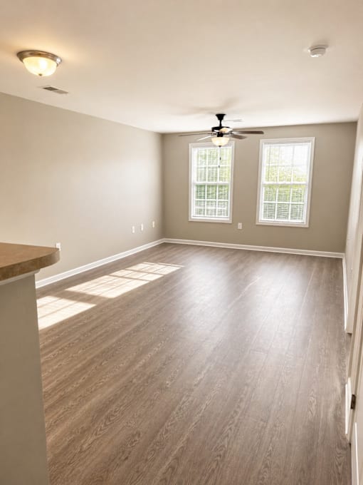 A room with a ceiling fan and two windows.