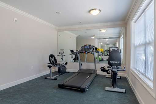 Well-lit fitness center equipped with treadmill, stationary bike, and mirrored wall designed for resident wellness at Snowden Senior Apartments.