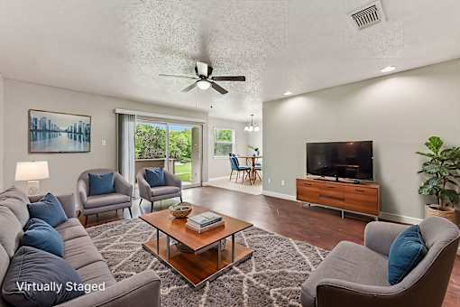 A living room with a grey couch, a coffee table, a television, and a ceiling fan.