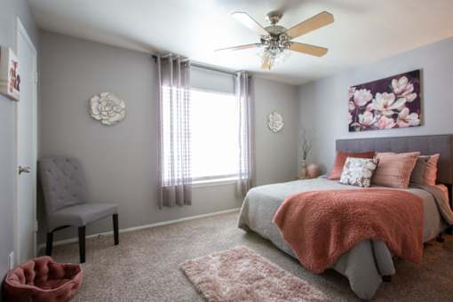A bedroom with a bed, chair, and a ceiling fan.