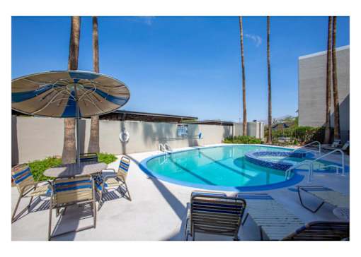 A pool surrounded by chairs and umbrellas with a building in the background.