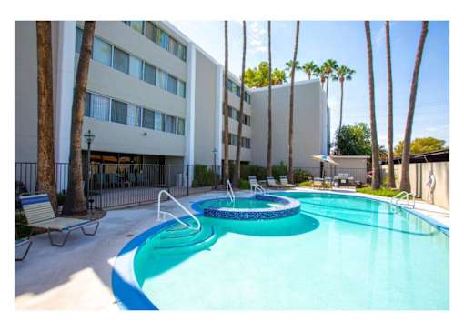 A swimming pool in front of a building with palm trees.