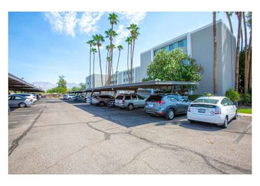 A parking lot with cars and palm trees in front of a building.