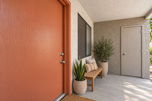 A brown door is on the left of a patio with a bench and potted plants.