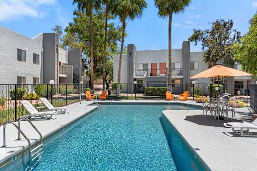 A swimming pool surrounded by chairs and trees in front of a building.