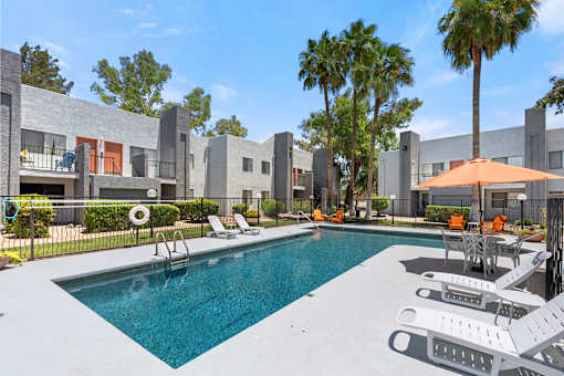 A swimming pool surrounded by lounge chairs and umbrellas in a sunny outdoor setting.