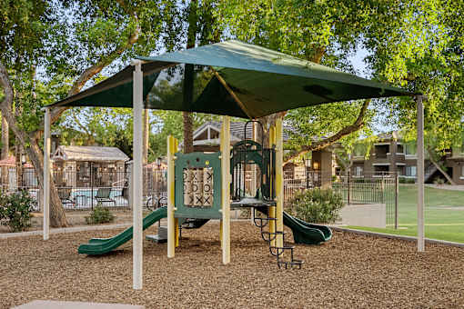 A playground with a green slide and a canopy.