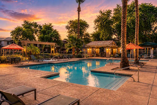 A pool surrounded by palm trees and lounge chairs.