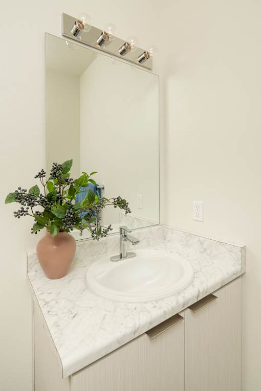 A bathroom sink with a pink vase and a mirror above it.