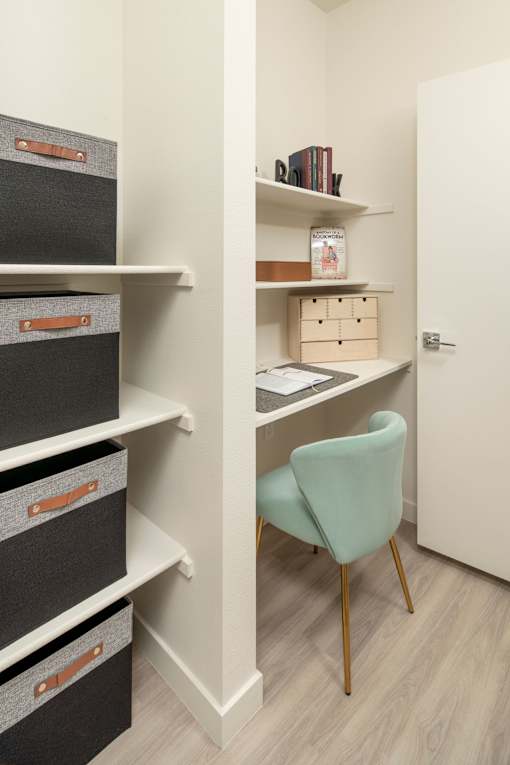 A white desk with a green chair and a white shelf with boxes and books.