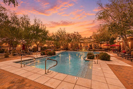 A swimming pool surrounded by trees and lounge chairs at sunset.