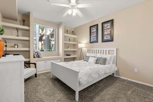 A bedroom with a large bed, a dresser, and a window with a view of trees.