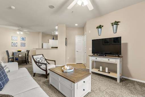 A living room with a white couch, a wooden coffee table, and a flat-screen TV mounted on the wall.
