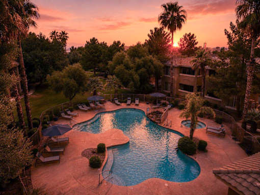 A beautiful sunset view of a pool surrounded by palm trees.
