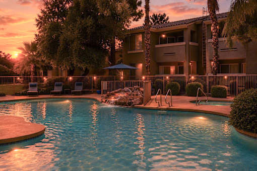 A pool surrounded by a fence and trees with a sunset in the background.