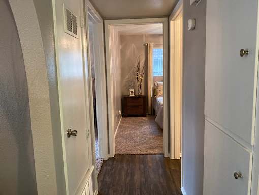 A hallway with a door on the left and a bedroom at the end.