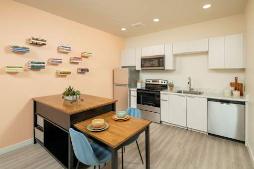 A kitchen with a table and chairs in the foreground and a refrigerator, oven, and microwave in the background.