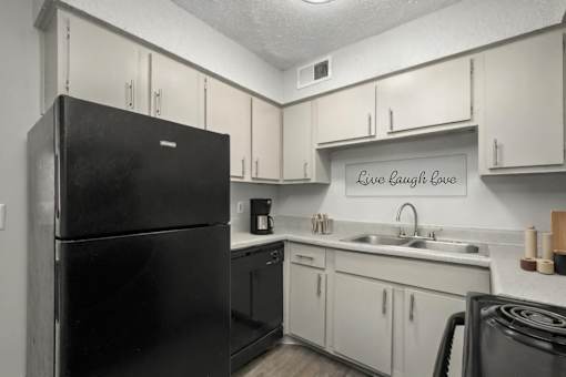 A black refrigerator in a kitchen with a sign that says Live Laugh Love.