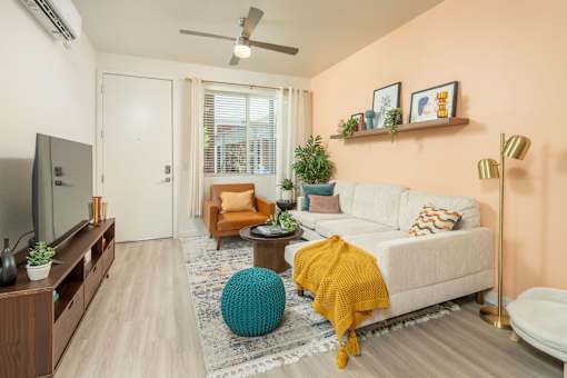 A living room with a white couch, a yellow throw blanket, and a blue pouf.