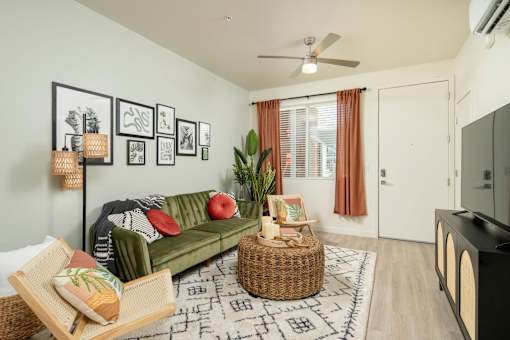 A living room with a green couch, a wicker table, and a fan on the ceiling.