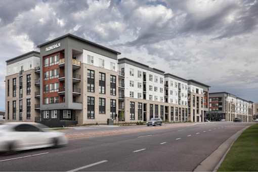 A white car is driving down a street past a building with a sign that says Lincoln.